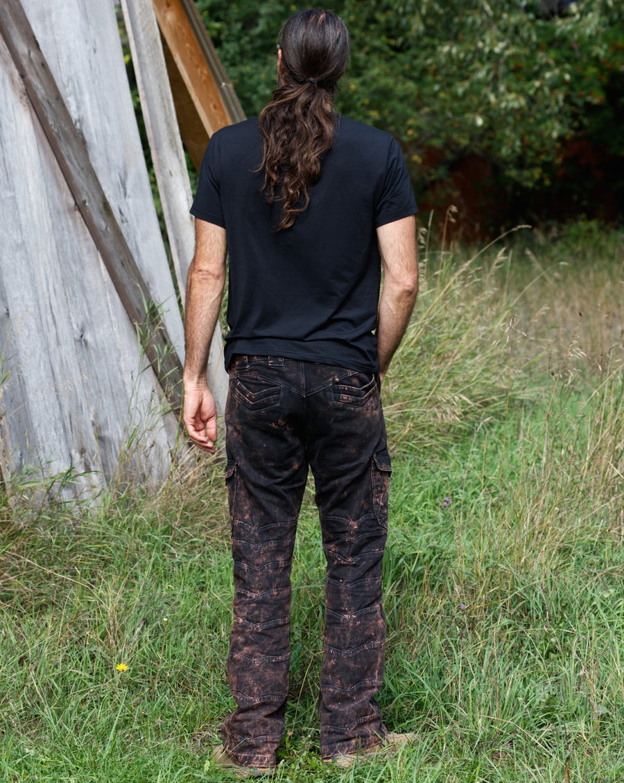 A tall, lean man is standing with his back to the camera while wearing a black t-shirt and rust coloured designer jeans.