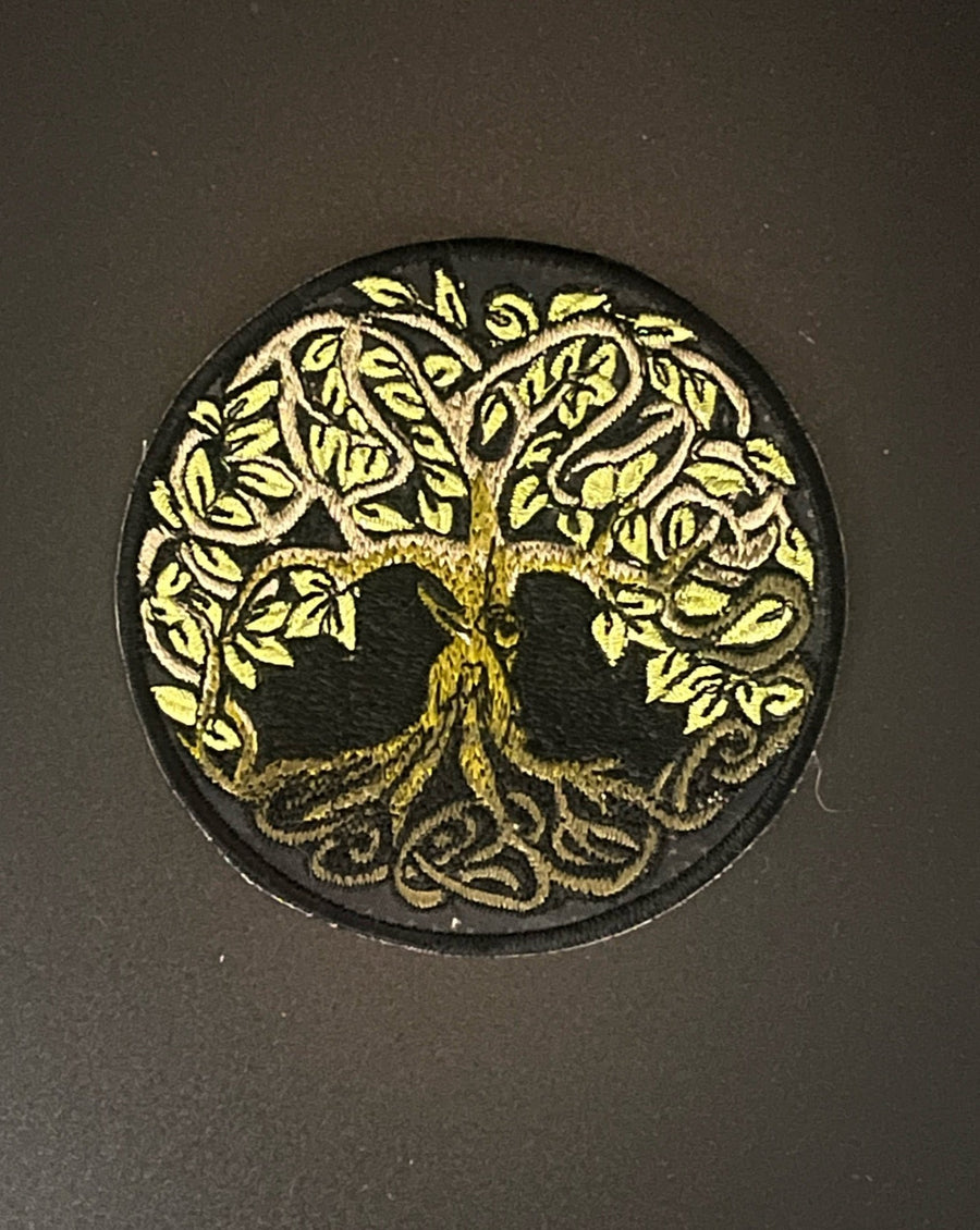 Hand embroidered tree of life patch in a green and black circle sits in the middle of a black background.