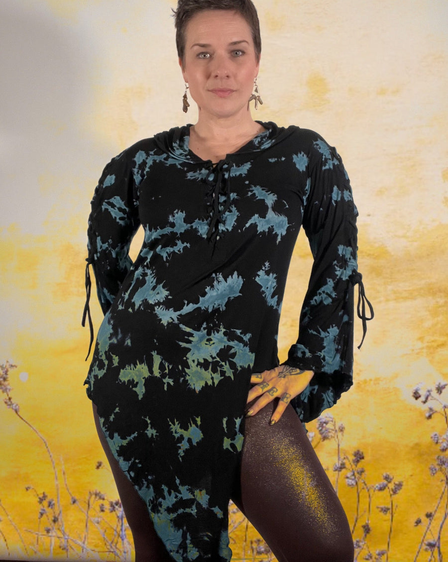 A white woman with short hair is standing with one hand on her leg while wearing a long dress with blue and black marble thai dye. There is an overlay of wild flowers giving the image a yellow hue and spring vibe.